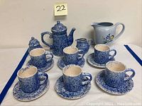 Blue and white sponge speckled coffee set including coffee pot, six cups and saucers, sugar bowl, creamer, and white Arabia floral pitcher arranged on a table.