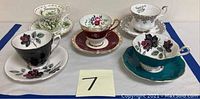 Five tea cups and saucers displayed on table, showing different floral and color patterns