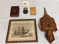 Photo showing four items of the lot: antique cast iron padlock, a small vintage paper booklet, a leather fireplace wood bellow, and a framed ship etching with artist signature.