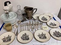 Wide shot showing entire lot with mixer, crystal decanter, stoneware monkey pitcher, silver pitcher, flatware, and ship plates arranged on table.