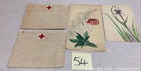 Three medic linens and two watercolor floral paintings visible together on table.