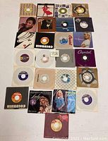 Photo showing an assortment of 27 vinyl 45 records including loose singles and some with original artist covers, arranged in a grid layout on a white surface.