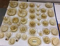 Full view of yellow depression glassware set showing bowls, cups, plates, a covered butter dish, glasses, and divided plates arranged on white cloth.