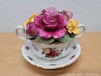 Porcelain cup and saucer with red, pink, and yellow ceramic roses forming a bouquet inside the cup. Classic Old Country Roses pattern with gold trim accents visible.