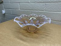 Front side view of vintage pink glass vase with open lattice rim and scalloped edges on a wood surface against a brick wall background.