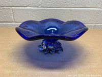 Side view of the cobalt blue Murano glass dish showing its wavy petal-shaped rim and silver-tone grape cluster base.
