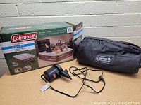 Coleman queen double high air bed box, electric pump, and black carrying/storage bag with Coleman logo.
