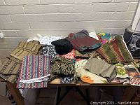 Photo showing a large assortment of folded and stacked fabric pieces with various colors and patterns on a table against a beige brick wall.