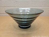 Side view of a large handmade glass bowl showing its conical shape, smoky tint, and ridges.