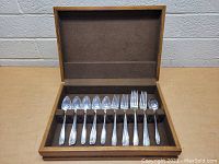Top-down view of open wood case containing 25 pieces of silverware arranged in rows.