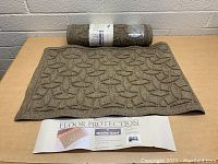 Two brown Weather Guard Floor Protection door mats, one unrolled with visible embossed geometric leaf-like pattern, and one rolled-up with product label visible.