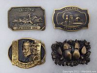 Four vintage brass belt buckles featuring various Arizona-related designs arranged on a surface.