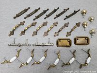 Overhead photo showing all assorted cabinet and drawer pulls and knobs arranged on a gray surface.