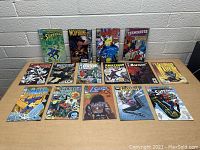 Photo showing 16 assorted DC and Marvel comic books laid out on table, covers visible showing characters including Superman, Wolverine, Batman, The Terminator and various Marvel heroes.