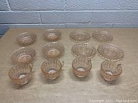 Group of assorted vintage pink glass dishes and cups arranged on a table, showcasing the variety of shapes and sizes including bowls and small plates with embossed patterns.