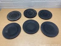 Top view of six black cast iron plates with circular textured patterns arranged on a wooden surface.