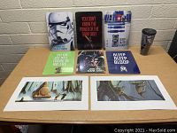 Overview of Star Wars collectibles including metal signs, artwork prints, and tumbler on table