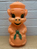 Front view of the orange plastic pig coin bank with detailed facial features and green bow