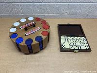 Poker chips in round cardboard holder and domino set in open wooden hinged case shown from above on tabletop.