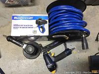 Top-down view showing all items including the blue air hose coiled on a reel, spot blaster gun box, stapler/nailer, and grinder on concrete floor.