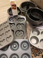 Selection of bakeware pans including Bundt cake pans, springform pans, pretzel and heart-shaped muffin pans, standard muffin pan on floor.