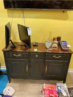 Full front view of black buffet cabinet with wood top and multiple decorative gold handles, holding two computer monitors and various items on top.