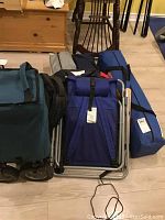 Various outdoor camping items including folded gazebo in blue bag, foldable chairs, utility cart, and backpacks.