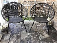 Front view of two black woven resin chairs with metal legs, positioned on stone flooring.