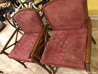 Pair of bamboo-framed armchairs with red leather upholstery on seat and backrest, positioned on wood-look floor showing some wear on the leather.