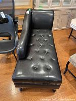 Full view of the black vinyl chaise lounge showing the tufted surface, armrest, and backrest.