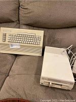 Commodore 64 computer with keyboard and Commodore 1541 disk drive on brown fabric couch.