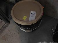 Top view of the bucket with a tan lid, showing sticker/title.