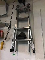 Image of an aluminum multi extension ladder folded and mounted on a wall next to other tools.