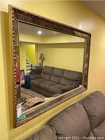 Full view of gold framed mirror mounted on yellow wall, reflecting living room furniture.
