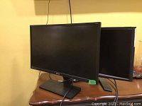 Two monitors on a wooden surface, Acer 23 inch behind BenQ 25 inch monitor, both with power cords