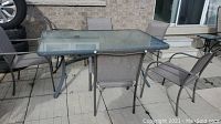 Full view of rectangular glass top patio table with six mesh fabric patio chairs surrounding it, set on outdoor patio.
