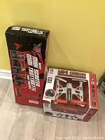 Mini Orion Live Feed LCD Screen Drone and Renegade Mini Trottinette scooter in original packaging, standing upright on a floor against the wall.