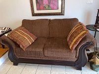 Front view of the brown fabric 2 seat sofa with two striped fringed cushions and dark wood frame.