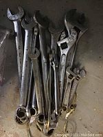 Photo showing the assortment of large sized combination wrenches and adjustable wrenches on a flat surface.