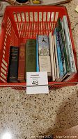Books in red shopping basket arranged showing spines and titles, including botany and gardening books of different sizes and conditions.