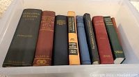 Photo showing nine antique medical books of various subjects and publication years in a plastic tote container.