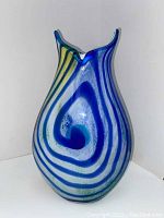 Front view of hand blown glass vase showing blue swirl design with yellow and green accents and flared top with two points.