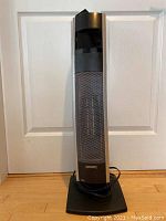 Full view of Bionaire tower heater against a white door, black base, power cord coiled at bottom.