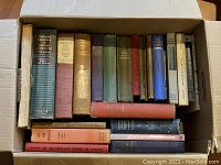 Top view photo showing a box filled with multiple hardcover books of various titles and colors, mostly English literature and one history book from 1873.