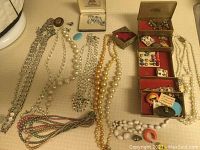 Full lot of costume jewelry including multiple necklaces in various colors and styles laid flat on fabric surface, with several pairs of earrings housed in small boxes.