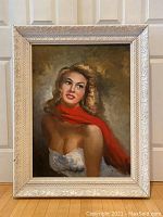 Full view of framed portrait painting of a blonde woman with a red scarf, showing frame and background.