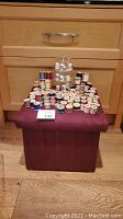Full lot setup showing vintage wooden spools of thread arranged on top of a burgundy ottoman with a clear dome display stand on top holding thimbles.