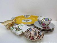 Group photo showing all porcelain items including the serving dish, bowls, pitcher, dessert cup, and saucers arranged together.