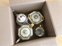 Items in a cardboard box showing teapots, cream, and sugar containers with octagonal shapes and floral pattern teapot