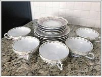 Five teacups arranged around a stack of plates and saucers showing floral and gold designs